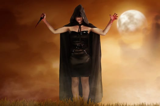 Young witch woman in black hooded cloak holding bloody knife with dramatic scene background