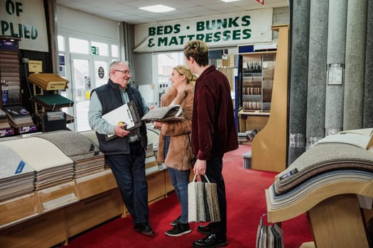 Young couple are discussing design ideas with a senior sales clerk in a carpet shop.