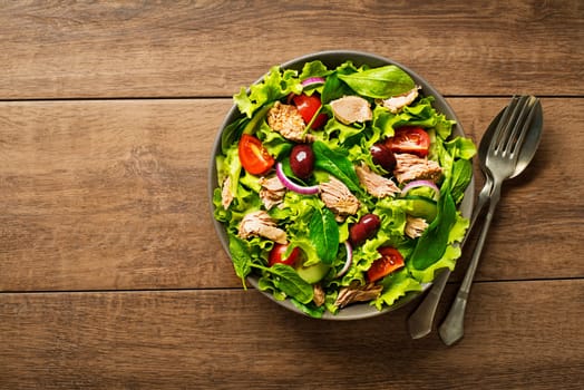 Tuna salad with lettuce, tomatoes and olives on wooden table