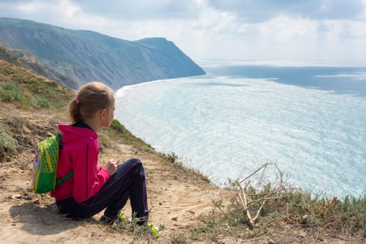 The girl sits on a high bank and looks at the sea
