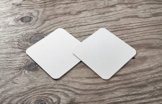 Blank white square beer coasters on wood table background.
