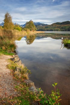 Wide-angle landscape view over the lake Weissensee with wooden bench on the left bank side and the first foothills of the high Alps in the background, near the city Fuessen.