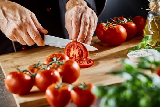 Close up on unidentified man slicing up small tomatoes on light brown wooden cutting board with metal knife