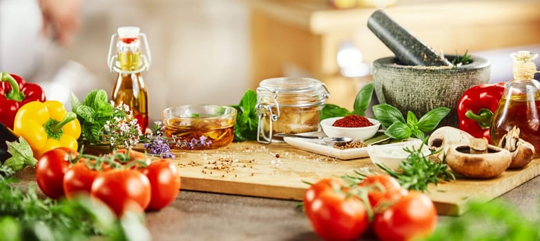 Panorama banner with fresh culinary herbs and spices on a chopping board with a pestle and mortar surrounded by fresh vegetables for salads