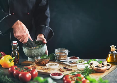 Chef with head out of camera view grinding herbs next to seasoning containers sitting on top of wooden cutting board