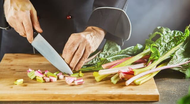 Man chopping fresh rhubarb chard, mangold or Swiss chard with a large chefs knife on a wooden chopping board
