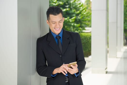 Young asian businessman using smartphone with relax outside office room