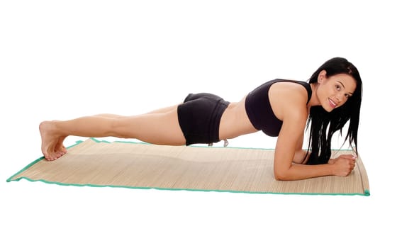A pretty young woman lying on her stomach in black sports outfit doing.push up's, looking into camera, isolated for white background.