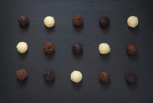 Fancy dark milk white chocolate truffles ready to eat on black stone background.