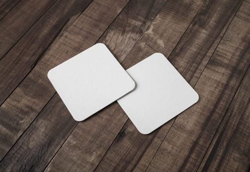 Two blank white beer coasters on vintage wooden background. Responsive design mockup.