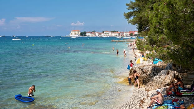bathing tourists on the beach of Porec in Croatia. In the background the old town.