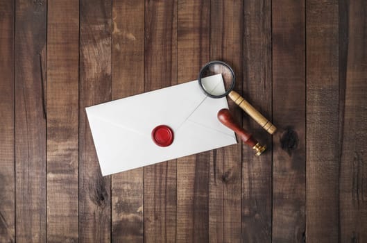 Blank paper envelope with wax seal, stamp and magnifier on wood table background. Mockup for your design. Flat lay.