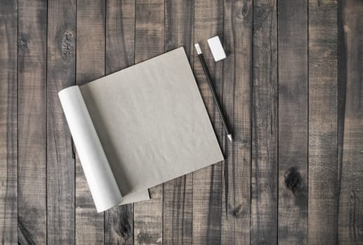 Open square format brochure or notepad, pencil and eraser on wooden table background. Flat lay.