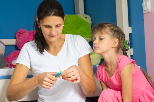 The daughter closely watches as her mother helps her cut out figures from colored paper
