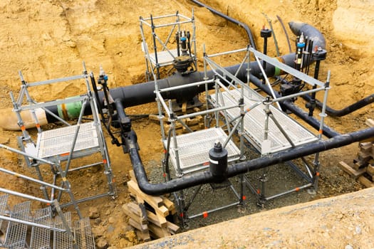Black piping running between metallic scaffolding and stairs inside deep hole in the ground with no people in sight