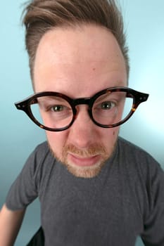 Man wearing large glasses stretching forwards to peer into the lens in a distorted perspective emphasising his eyes and glasses in a fun portrait