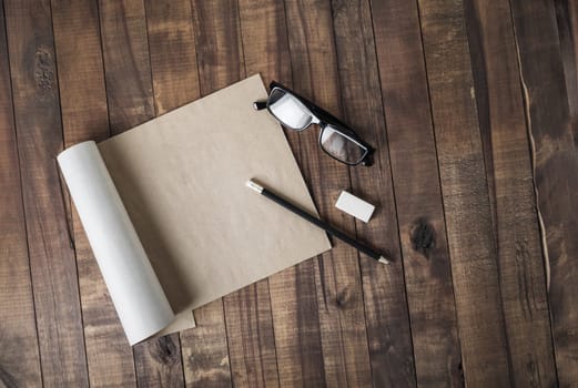 Blank notepad or brochure of kraft paper and stationery: glasses, pencil and eraser on vintage wooden background. Responsive design mockup. Flat lay.