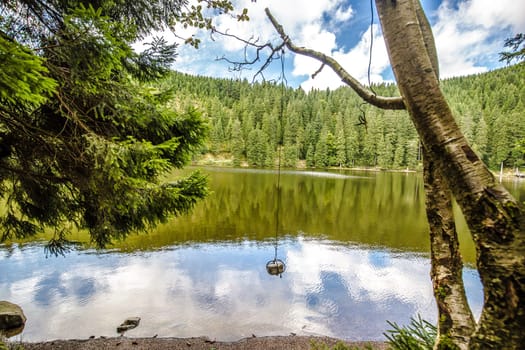 Tranquil mountain lake with reflections of the surrounding green forests viewed from a rocky shoreline on a sunny cloudy day