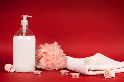 White shower gel, towel, bath sponge, flower and candles are on red background.