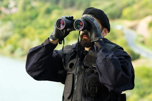 The security man in uniform is looking away with binoculars outdoor in nature.