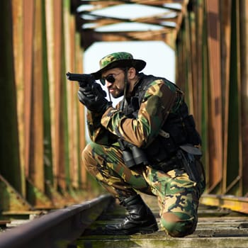 The soldier in military uniform is aiming with handgun on old bridge.