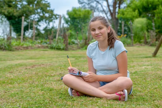 a young and smiling teenager sitting cross-legged in the grass