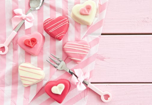 Colorful Petit Fours in heart shape on pink wooden background