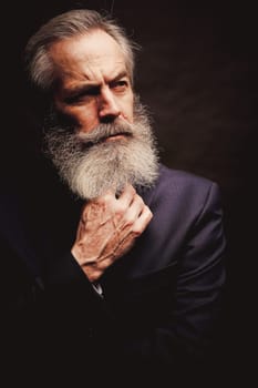 close up of senior man with grey hair and full beard, wearing suit on dark background