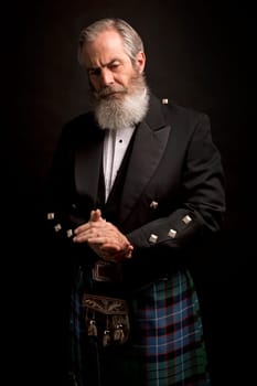 close up of senior man with grey hair and full beard, wearing scotting kilt on dark background