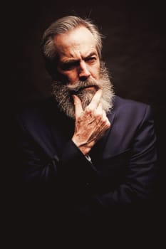 close up of senior man with grey hair and full beard, wearing suit on dark background