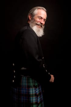 close up of senior man with grey hair and full beard, wearing scotting kilt on dark background