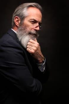 close up of senior man with grey hair and full beard, wearing suit on dark background