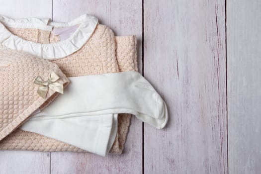 Top view on stack of colorful clothes for girl on a bright rustic wooden table. Space for your product display montage. Concept advertising and shopping children fashion.