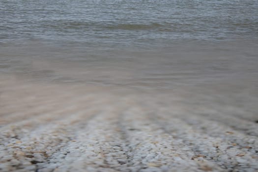 Water background texture with soft waves and white stones in foreground. Space for text.