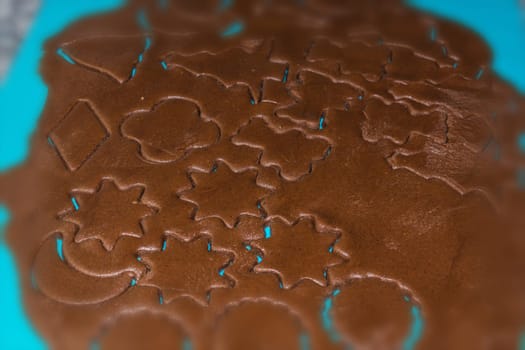 Raw dough is being punched out for the holiday cookies on a blue underlay. Preparing gingerbread cookies. Steps to making biscuits. Top view.
