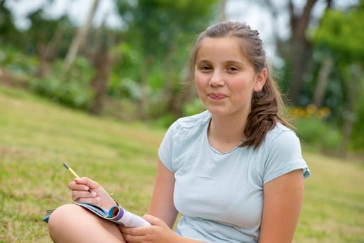 a young and smiling teenager sitting cross-legged in the grass