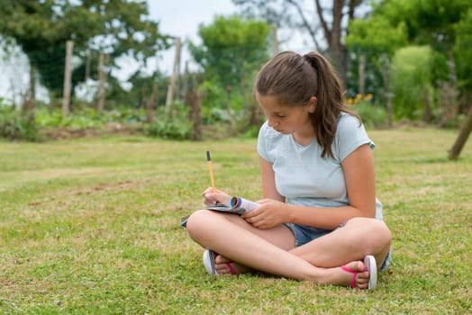 a young teenager sitting and writing cross-legged in the grass