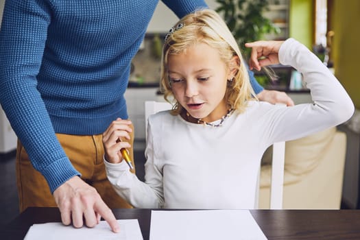 Father helping daughter with homework for elementary school at home.