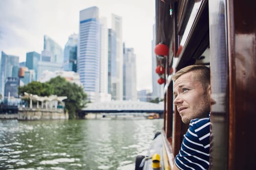 Young man exploring city and looking out from river boat in Singapore.