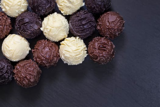 Delicious chocolate truffles on black stone background. Assortment of fine chocolates in white dark and milk chocolate.