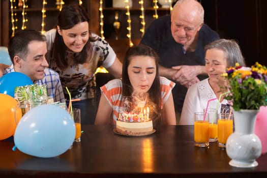 Happy family celebrating teenager daughter and granddaughter anniversary. The girl blows the candles on birthday cake. People hapiness and celebrating concept.