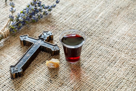 Taking communion with glass of wine and bread near cross and lavanda on the textile tablecloth.