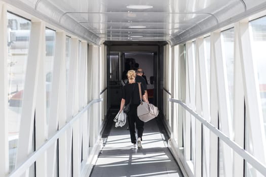 Airplane Boarding. Casual female passenger carrying the hand luggage bag, walking the airplane boarding corridor.