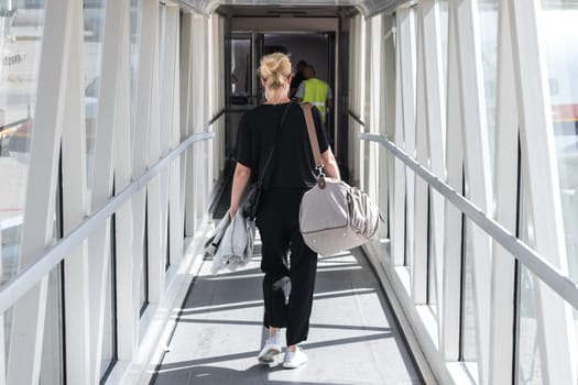 Airplane Boarding. Casual female passenger carrying the hand luggage bag, walking the airplane boarding corridor.