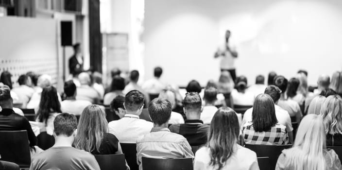 Speaker giving a talk in conference hall at business event. Focus on unrecognizable people in audience. Business and Entrepreneurship concept. Black and white image.