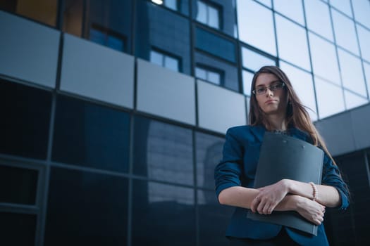 Successful beautiful young business woman standing against a background of buildings and holding folder.