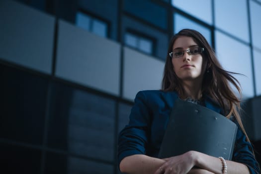 Successful beautiful young business woman standing against a background of buildings and holding folder.
