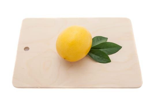 yellow lemon with three green leaves on a chopping board