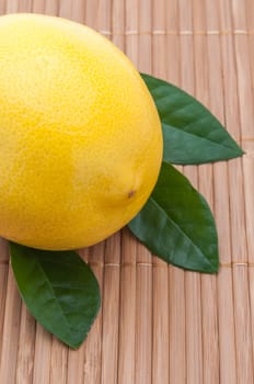 large yellow lemon with green leaves close-up on bamboo mat.