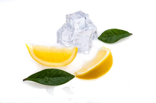 Cubes of cold ice, two slices of fresh lemon and green leaves on white isolated background.